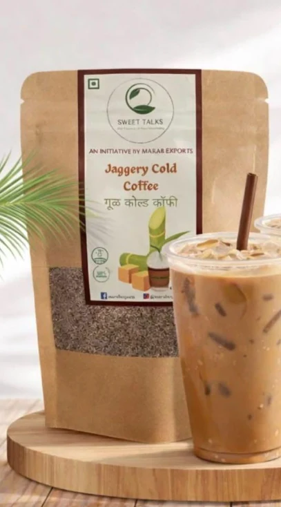 Sweet Talks Jaggery Cold Coffee pouch beside a tall iced coffee on a wooden board.