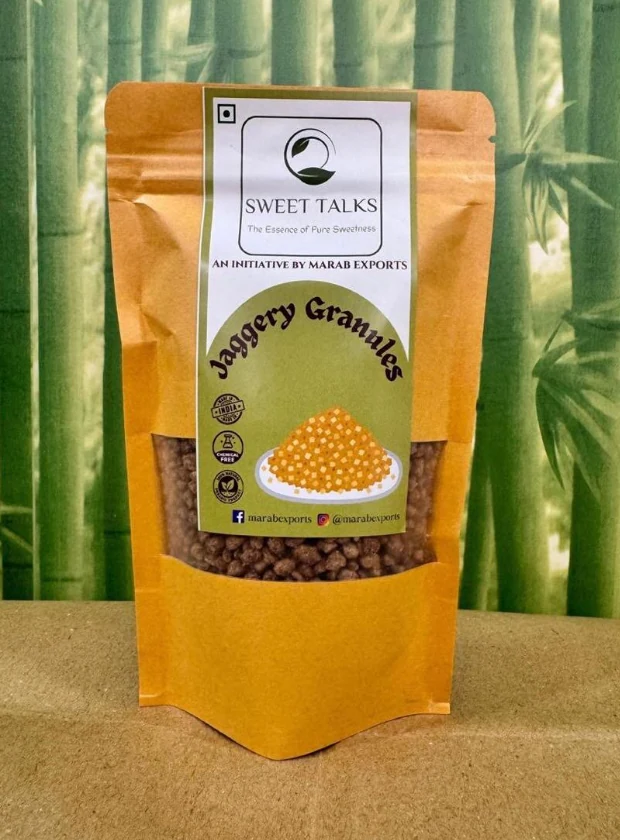 Sweet Talks Jaggery Granules in a kraft stand-up pouch with a clear window, photographed against bamboo.