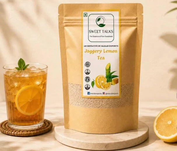 Sweet Talks Jaggery Lemon Tea pouch beside a tall glass of iced lemon tea and fresh lemons.